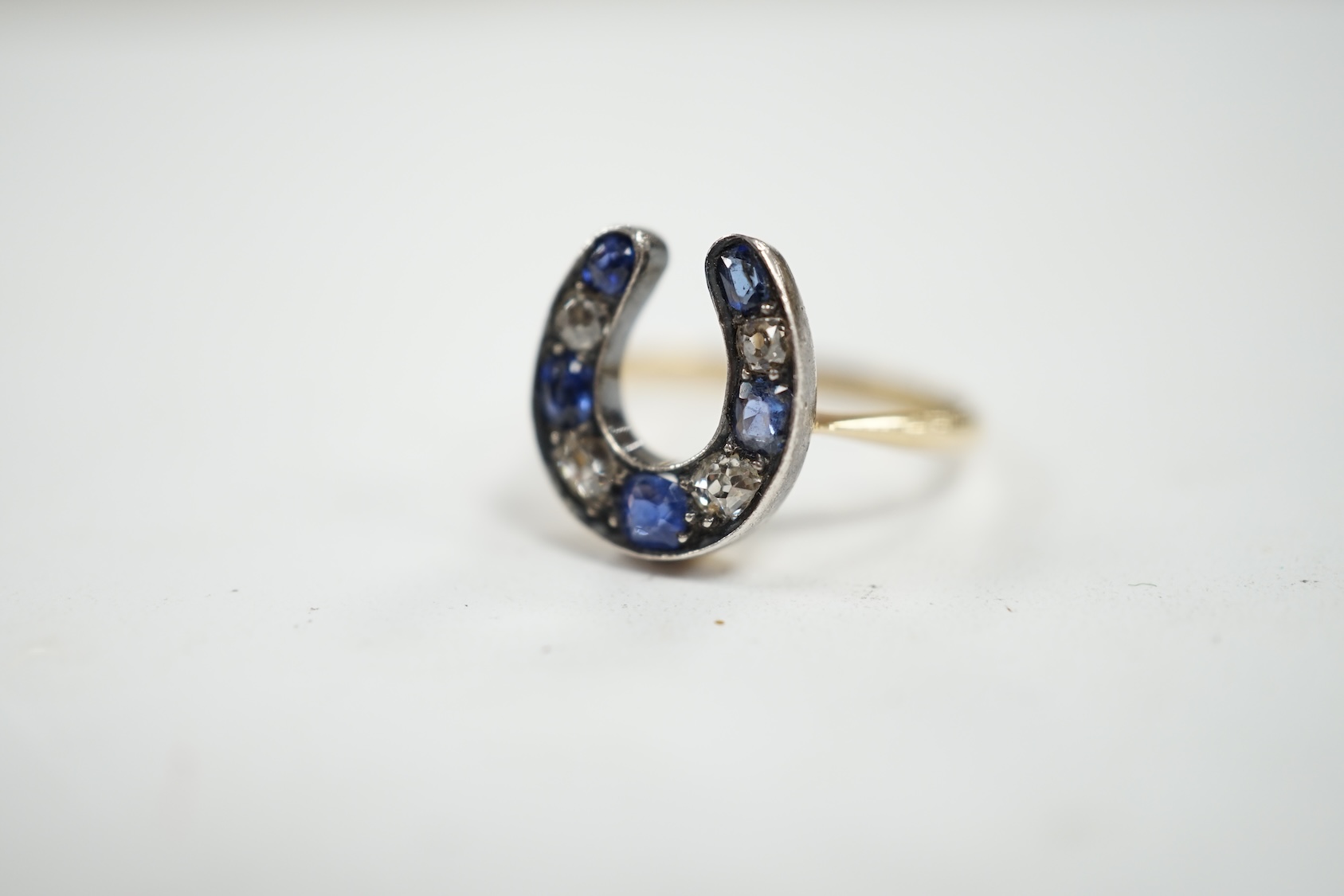 An early 20th century yellow metal (stamped 15), sapphire and diamond cluster set horseshoe shaped ring, size M, gross weight 2.8 grams. Condition - poor to fair